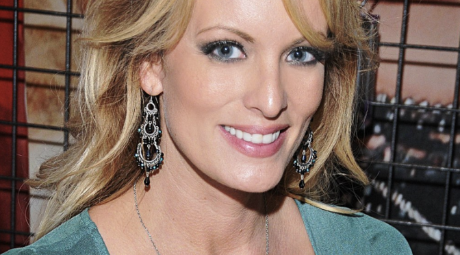 Stormy Daniels, probably in her 30s in this photo, wears a green top with a sweetheart neckline. She smiles at the camera.