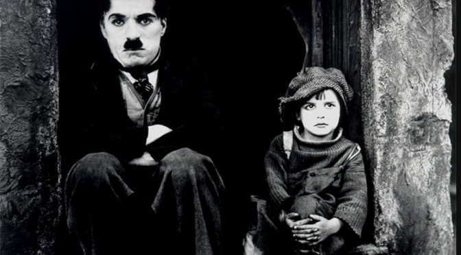 A black and white photo of Charlie Chaplin and child star Jackie Coogan dressed in rags in their characters of The Little Tramp and The Kid in the movie "The Kid."